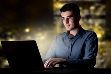 Young handsome businessman working late at night in the office with city lights in the background