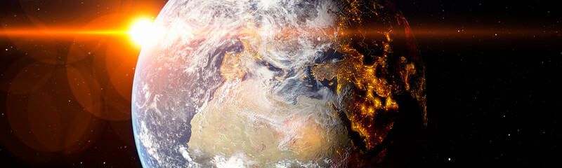 Fototapeta premium Earth from space with bright sun flare and city lights in the shadows panoramic