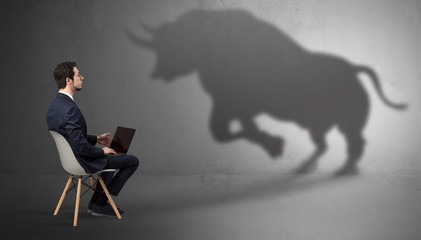 Humble businessman staying and offering stuffs to a huge angry bull shadow