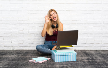 Teenager girl sitting on the floor with her laptop showing ok sign and thumb up gesture