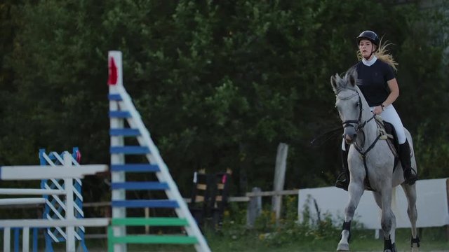 Young woman on horse jumping over obstacles. Slow motion. Training horses before the competition. Horse Racing. Horse breeding. Farm. Horseman. Rider, equestrian, jockey.