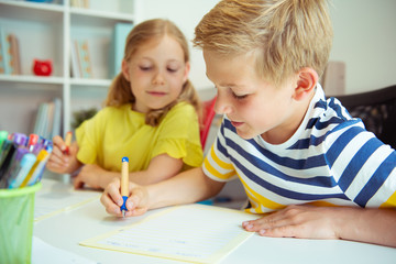 Cute schoolchildren are came back to school and learning at the table in classroom