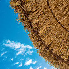Straw sun umbrella at the beach against blue sky.