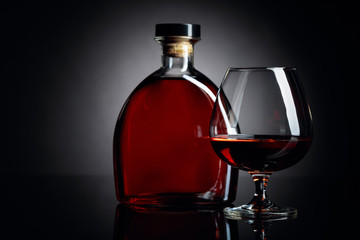 Glass and bottle of brandy on a black reflective background.