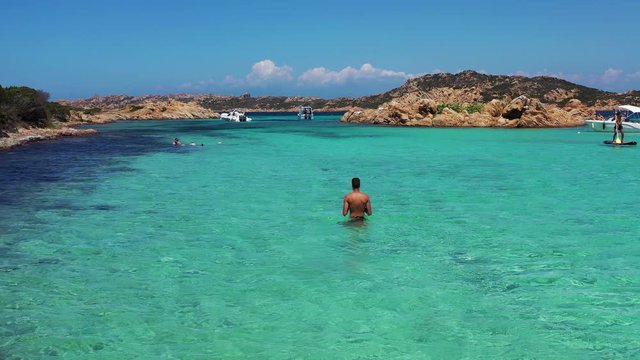 Young Man walking in water in La Spiaggia di Santa Maria beach in La Maddalena archipelago, Sardinia, Italy