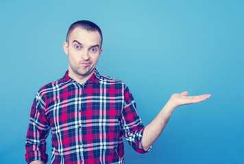 Dissatisfied young man points to the empty space, front view, blue background, copy space