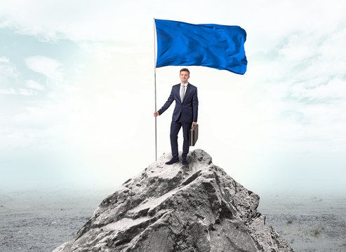 Handsome businessman on the top of the mountain with blue flag