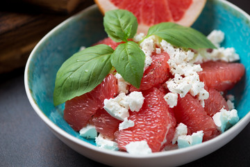 Salad with grapefruit, feta cheese and fresh green basil served in a turquoise bowl, closeup,...