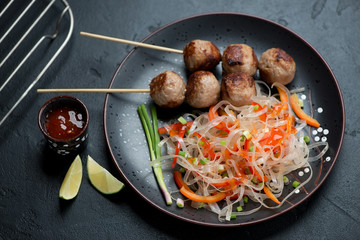 Plate with vietnamese nem nuong and pho noodles, studio shot on a black stone background