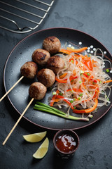 Nem nuong or fried vietnamese pork sausages on skewers served with pho noodles, vertical shot on a black stone background