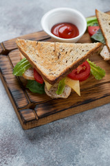 Sandwich with grain bread, chicken fillet, cheese and vegetables, studio shot on a beige stone background