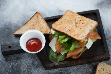 Sandwich with grain bread, salmon fillet, cheese and vegetables on a black wooden serving tray, horizontal shot