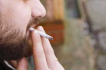 Portrait of brutal hipster adult working man after labor day with a beard close up smoking...