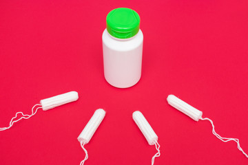 Tampons and white container of medicine on a red background, top view, close up