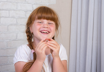 Little red-haired girl in a white dress holds a plate in her hands to correct a bite of teeth