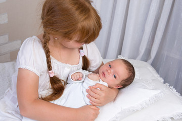 Little red-haired girl holding a newborn baby in her arms