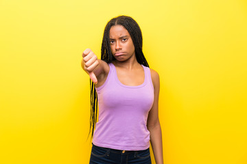 African American teenager girl with long braided hair over isolated yellow wall showing thumb down with negative expression