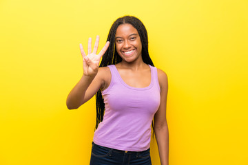 African American teenager girl with long braided hair over isolated yellow wall happy and counting four with fingers