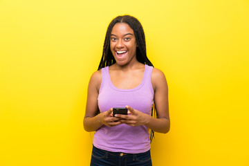 Naklejka premium African American teenager girl with long braided hair over isolated yellow wall surprised and sending a message