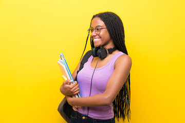 African American teenager student girl with long braided hair over isolated yellow wall looking to the side