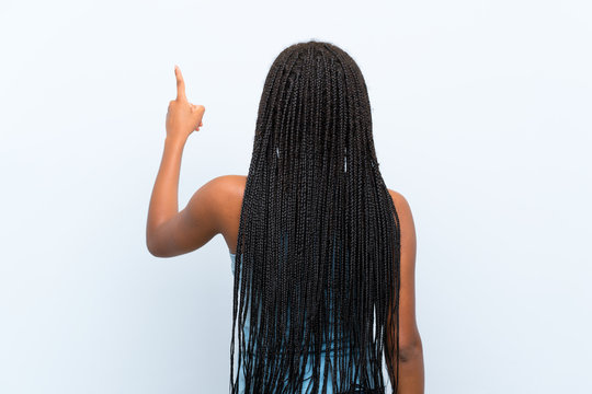 African American teenager girl with long braided hair over isolated blue background pointing back with the index finger