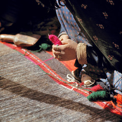 Afghanistan, Shibar Pass. Shadows highlight the detail of a weaver's hand and yarn at a loom on the...