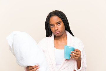 African American teenager girl with long braided hair in pajamas over isolated background and holding a cup of coffee