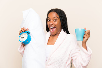 African American teenager girl with long braided hair in pajamas over isolated background and holding a cup of coffee