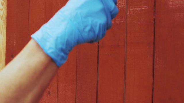 The painter paints a wall or a fence of wooden slats with brown or red alkyd paint using a roller. Close up.
