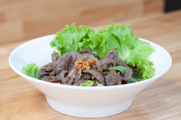 Chinese meat nooddle with green lettuce topping with roasted garlic in white bowl on wooden table.