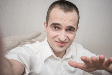 Unsatisfied man in white shirt makes a video call and gesticulates, sitting at home on the couch,...