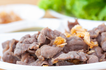 Fresh scalded meat serve with deep fried garlic and spicy sauce in white plate.