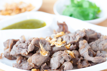 Fresh scalded meat serve with deep fried garlic and spicy sauce in white plate.