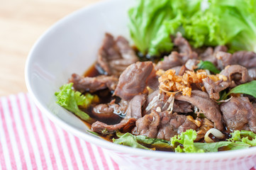 Chinese premium beef noodle with green lettuce topping with roasted garlic in white bowl on wooden table.