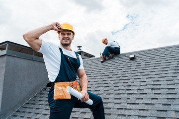 selective focus of happy repairman holding rolled paper while coworker repairing roof © LIGHTFIELD STUDIOS