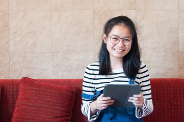 Asian teenager 16 years old wear eye glasses be happy holding her tablet pc with smile.