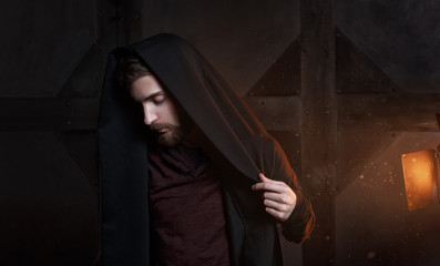 Caucasian white guy in a black cloak hood with gold rim light. Mystery concept