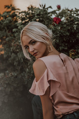  Beautiful girl on a background of a blossoming tree. Tender girl in rose petals. Flower scent. Stylish blonde in nature. Big earrings on a beautiful girl. Rose Extract