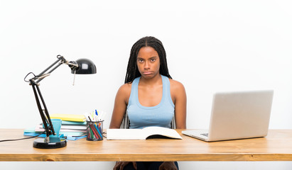 African American teenager student girl with long braided hair in her workplace with sad and depressed expression