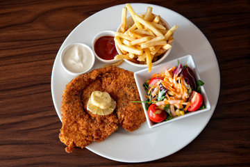 Herb crusted schnitzel with fresh lemon and herb butter on top on white plate. French fries and fresh garden salad on the side. Ketchup and mayonnaise dipping sauces. Taken in Izmir, Turkey.