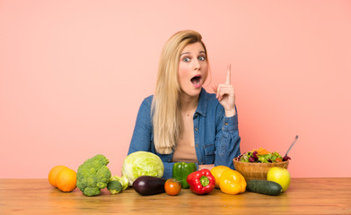 Young blonde woman with many vegetables thinking an idea pointing the finger up