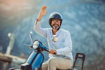 Mature man driving motor scooter in marina near the sea.