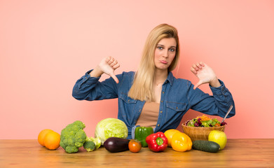 Young blonde woman with many vegetables showing thumb down