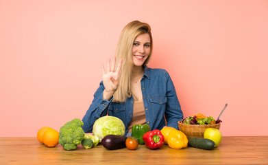 Young blonde woman with many vegetables happy and counting four with fingers