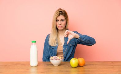 Young blonde woman with bowl of cereals showing thumb down sign