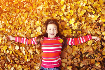 beautiful smiling teenage girl lying on yellow leaves in autumn. top view.
