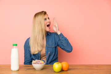 Young blonde woman with bowl of cereals shouting with mouth wide open
