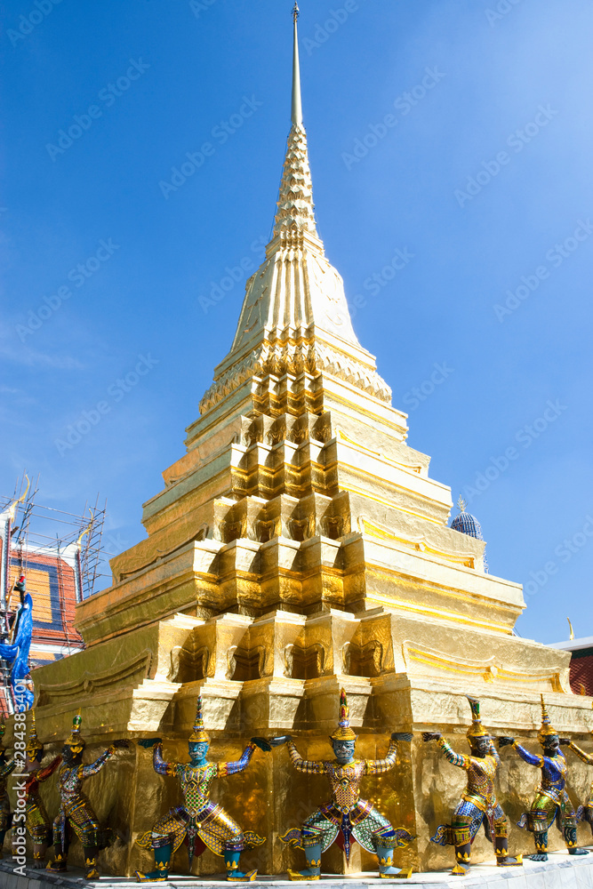 Sticker Bangkok, Thailand - Golden statues are holding a golden tiered building over their head. The tiered building terminates in a spire.