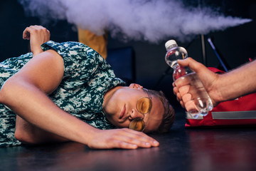 man in sunglasses lying on floor near bottle of water in nightclub