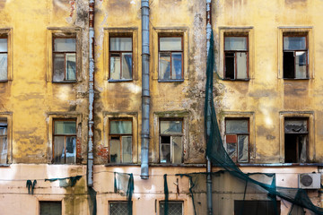 Exterior of an abandoned old residential building with broken windows with scraps of green plastic mesh on the wall